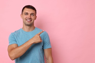 Smiling man with dental braces pointing at something on pink background. Space for text