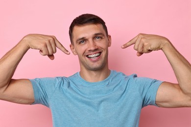 Happy man pointing at his dental braces on pink background