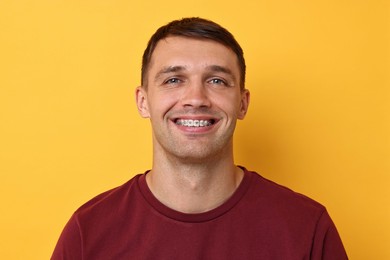 Smiling man with dental braces on yellow background