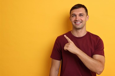 Photo of Smiling man with dental braces pointing at something on yellow background. Space for text