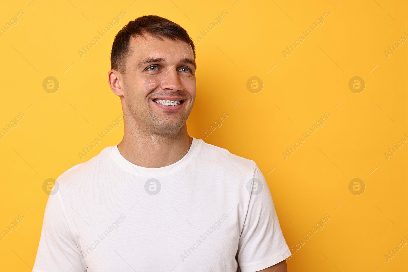 Photo of Smiling man with dental braces on yellow background. Space for text