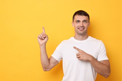 Photo of Smiling man with dental braces pointing at something on yellow background. Space for text