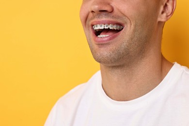 Photo of Happy man with dental braces on yellow background, closeup. Space for text