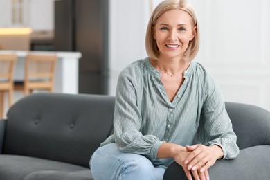 Photo of Happy middle aged woman on sofa indoors, space for text