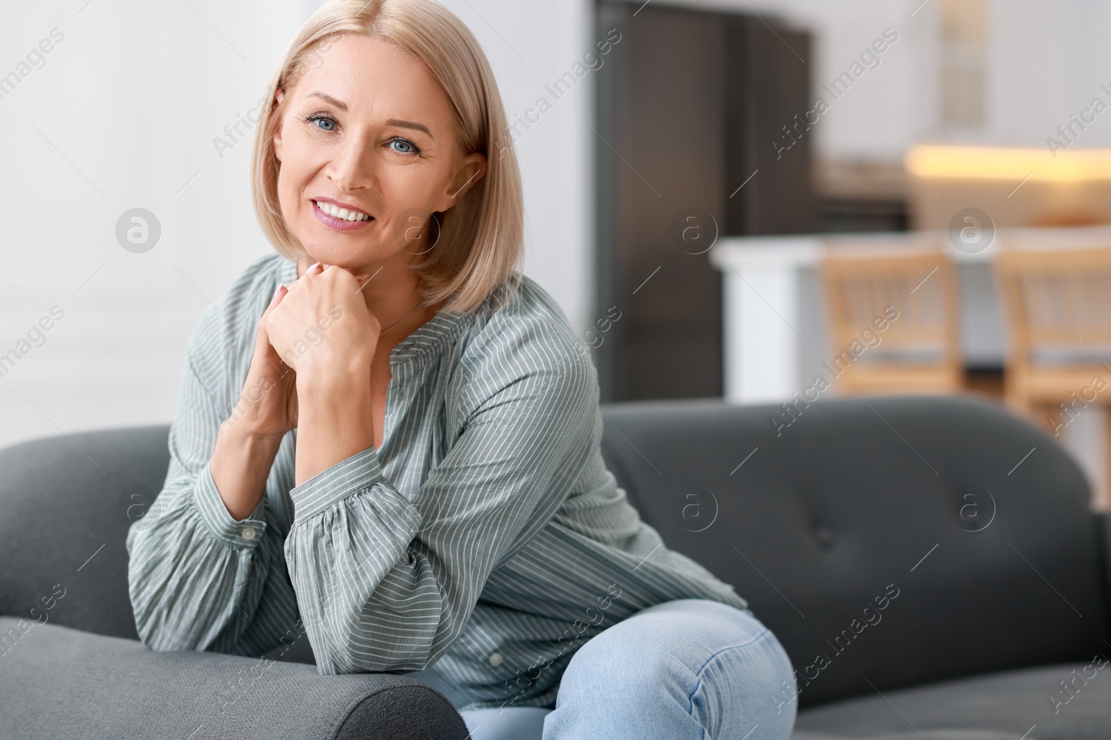 Photo of Happy middle aged woman on sofa indoors, space for text