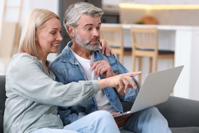 Happy middle aged couple using laptop on sofa indoors