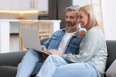 Happy middle aged couple using laptop on sofa indoors