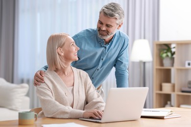 Photo of Happy middle aged couple working with laptop at table indoors