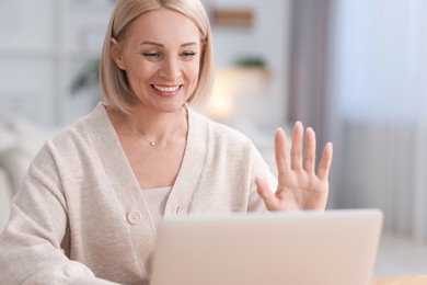 Happy middle aged woman having video chat via laptop indoors