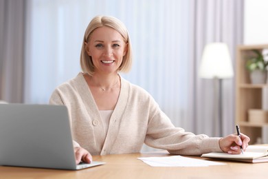 Happy middle aged woman working at table indoors