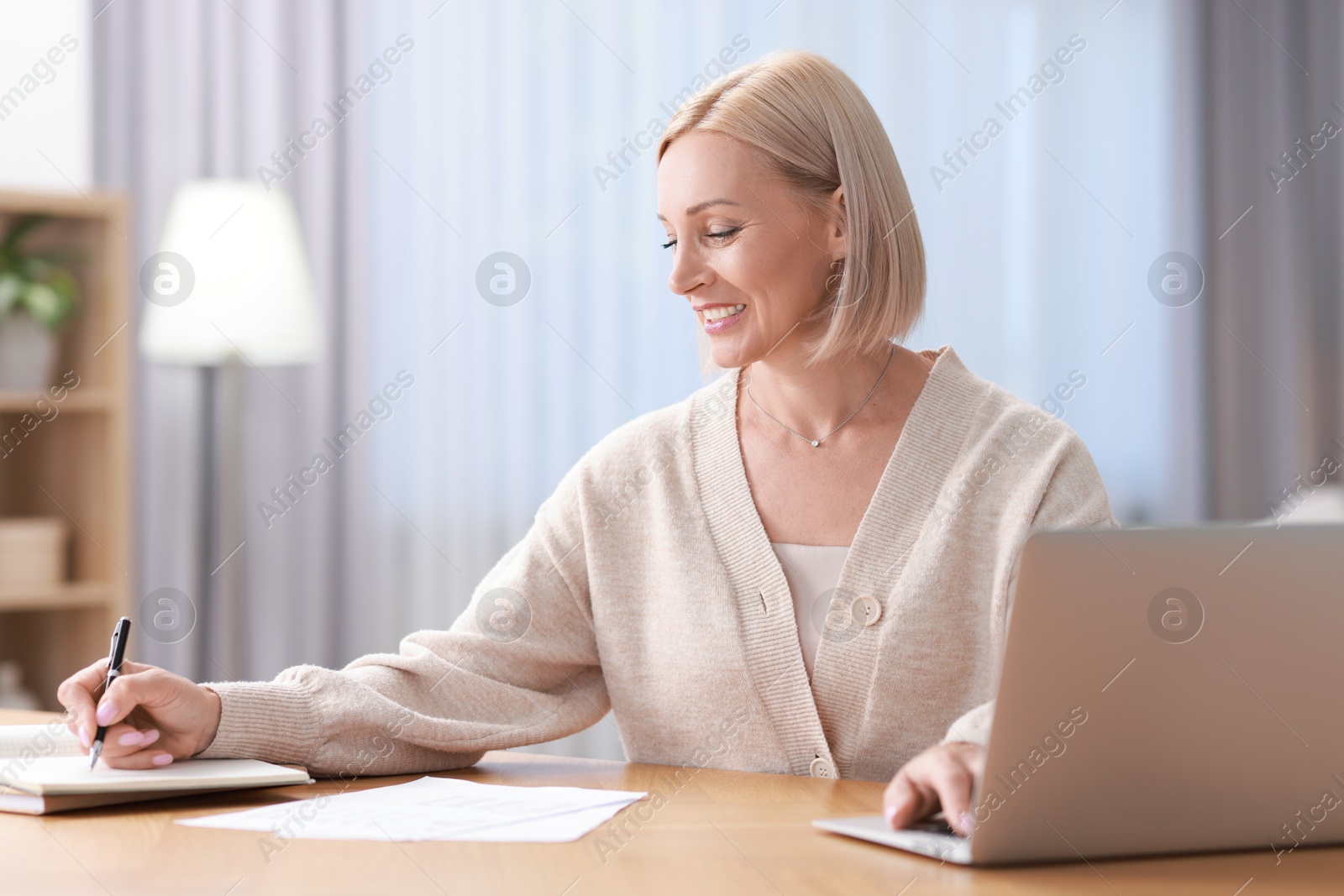 Photo of Happy middle aged woman working at table indoors