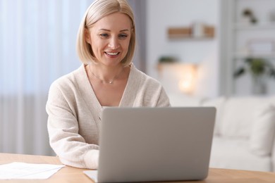 Photo of Happy middle aged woman using laptop at table indoors