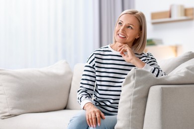 Photo of Happy middle aged woman on sofa at home, space for text