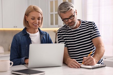 Middle aged couple working at white marble table in kitchen