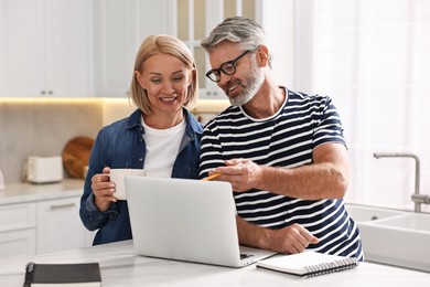 Photo of Happy middle aged couple working at white marble table in kitchen