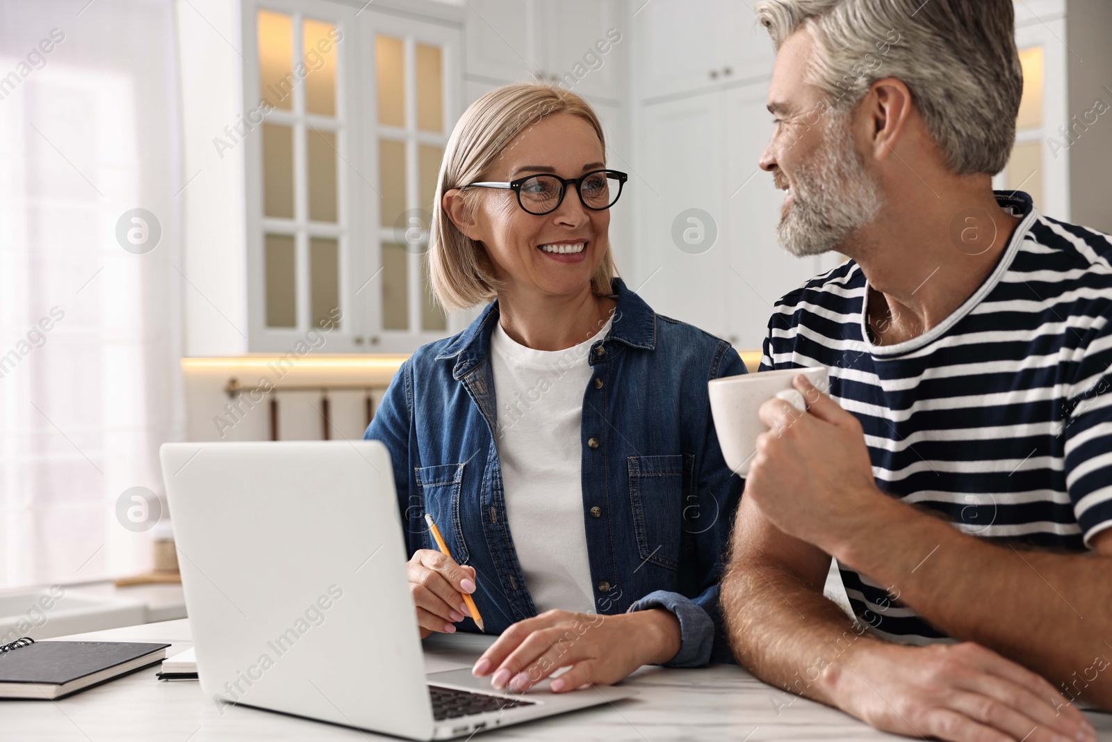 Photo of Happy middle aged couple working at white marble table in kitchen