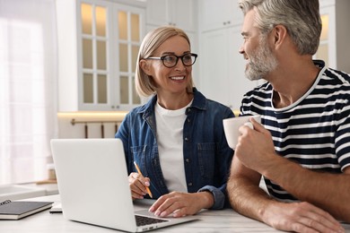 Photo of Happy middle aged couple working at white marble table in kitchen