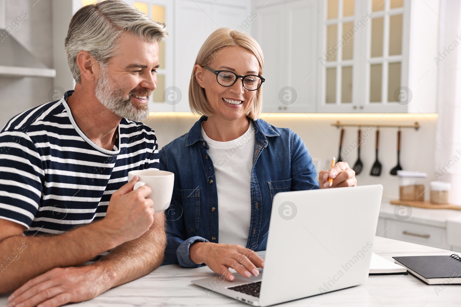 Photo of Happy middle aged couple working at white marble table in kitchen