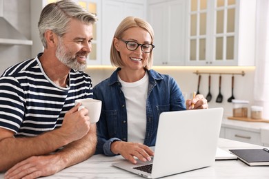 Happy middle aged couple working at white marble table in kitchen