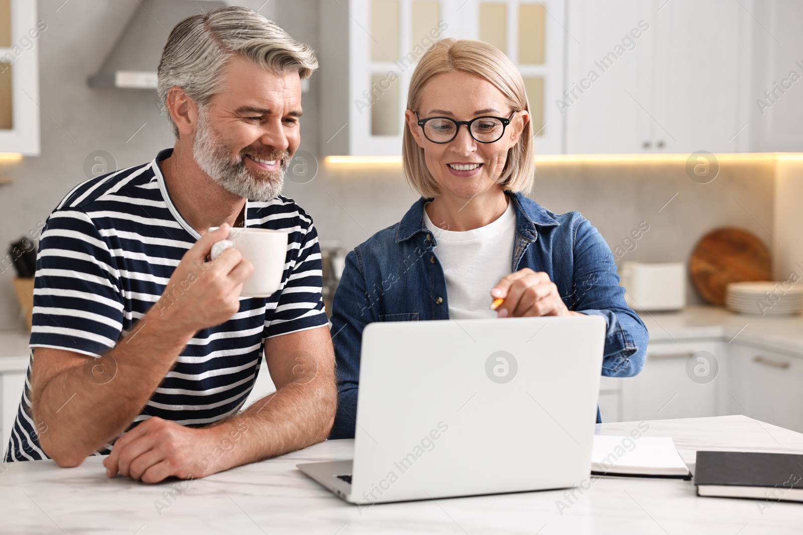 Photo of Happy middle aged couple working at white marble table in kitchen