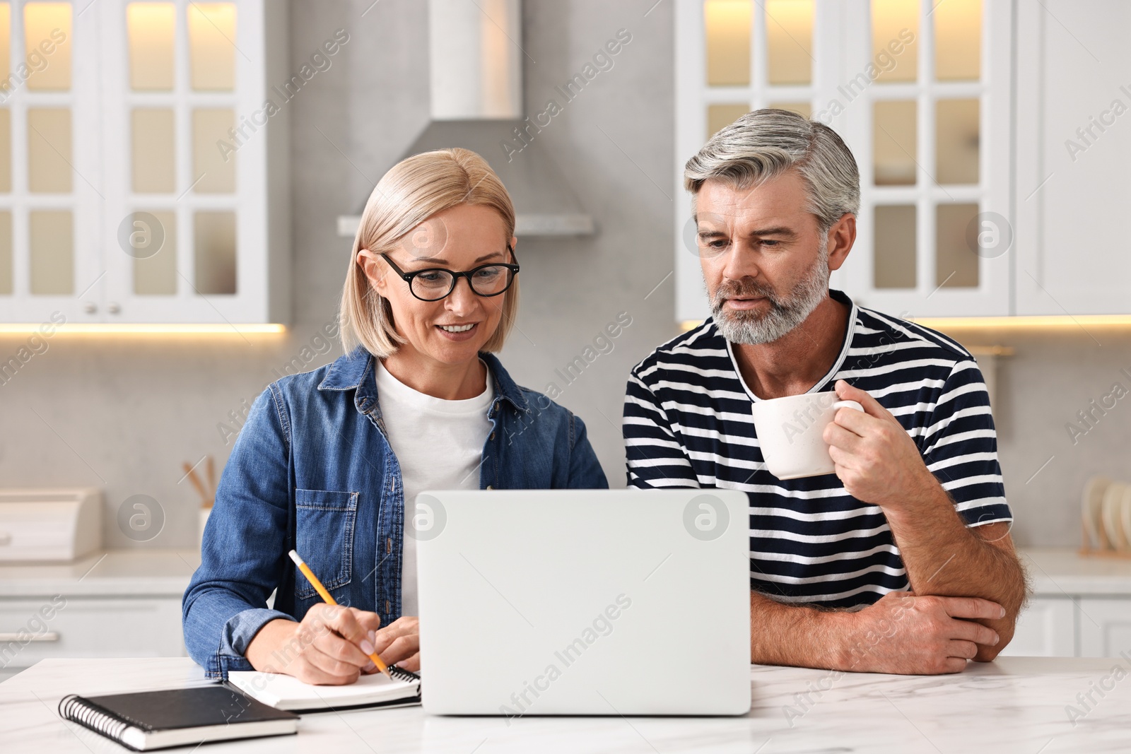 Photo of Middle aged couple working at white marble table in kitchen