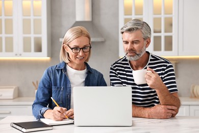 Middle aged couple working at white marble table in kitchen