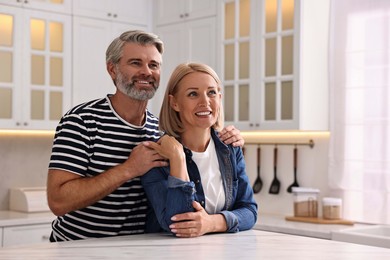 Happy middle aged couple at white marble table in kitchen