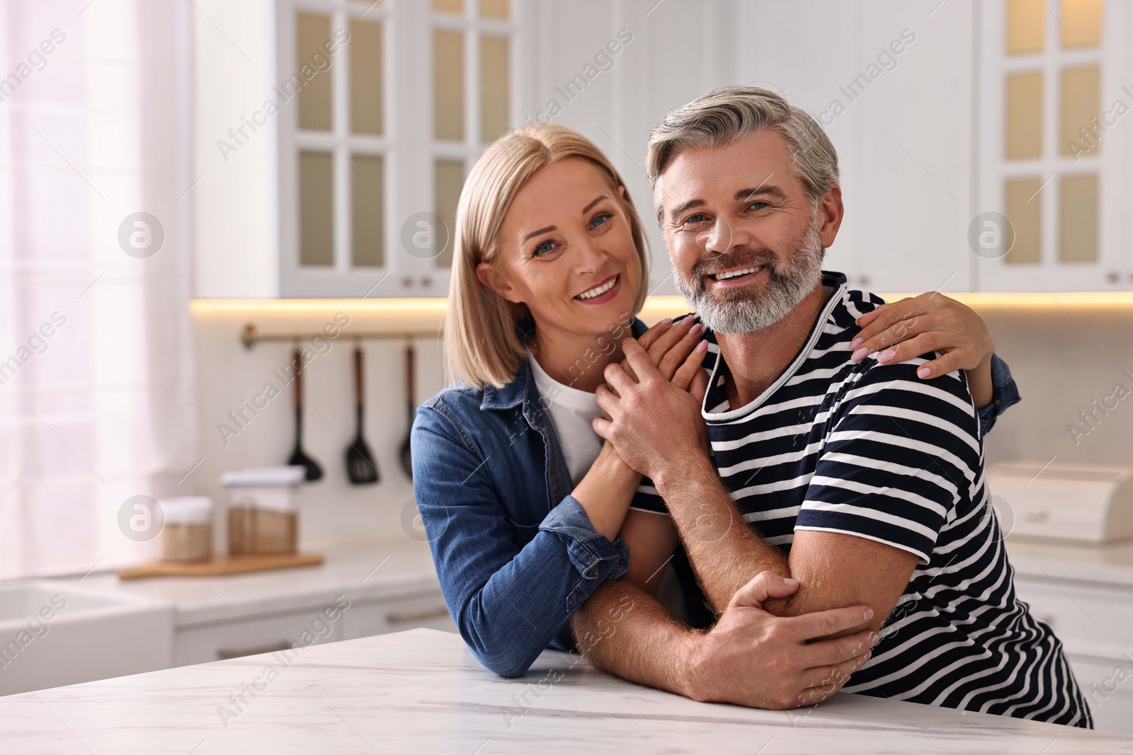 Photo of Happy middle aged couple at white marble table in kitchen