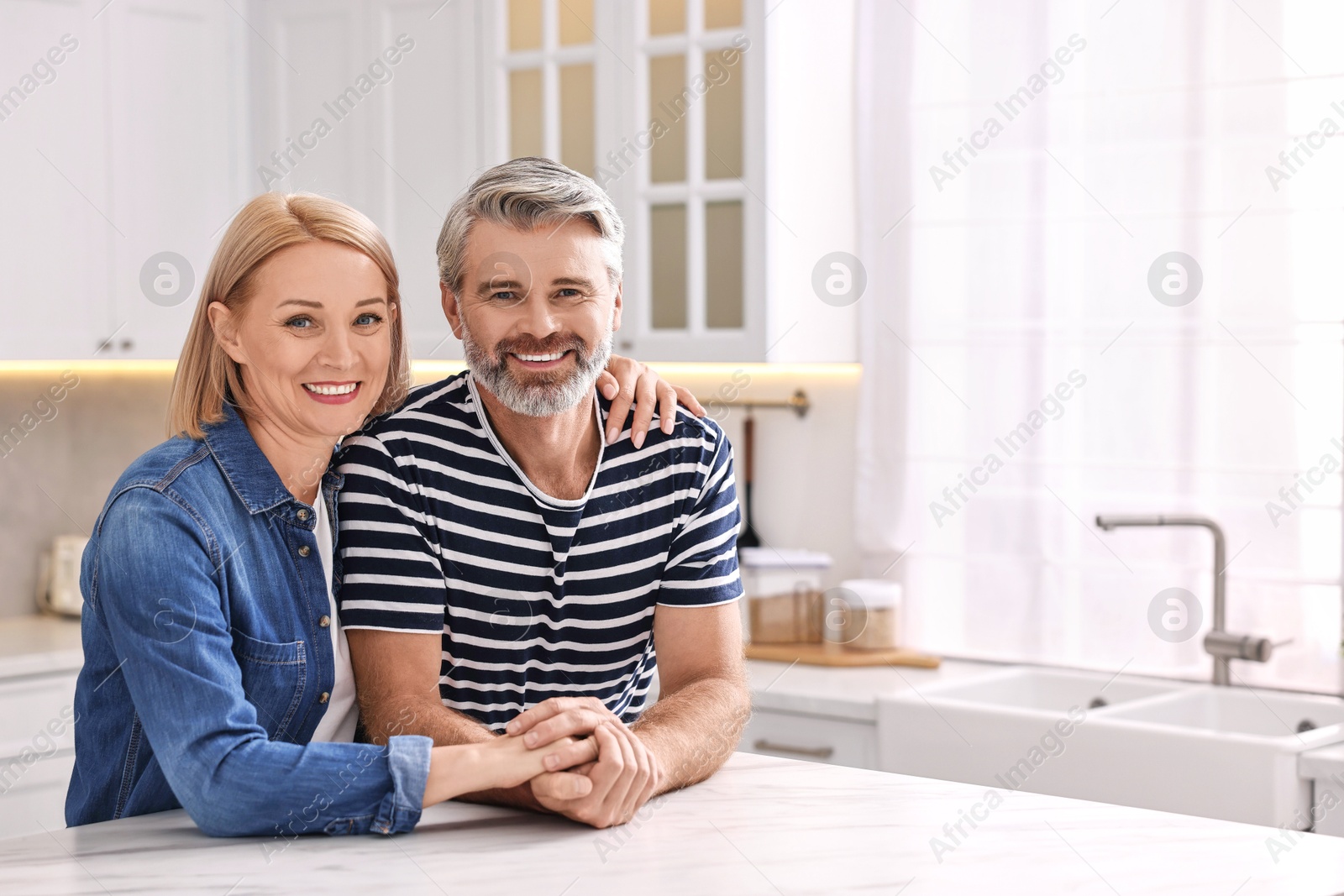 Photo of Happy middle aged couple at white marble table in kitchen, space for text