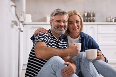 Happy middle aged couple with cups of drink in kitchen