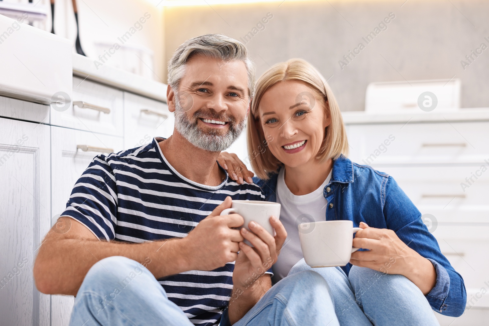 Photo of Happy middle aged couple with cups of drink in kitchen