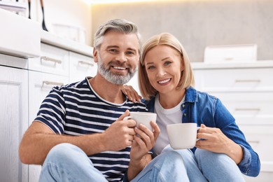 Happy middle aged couple with cups of drink in kitchen