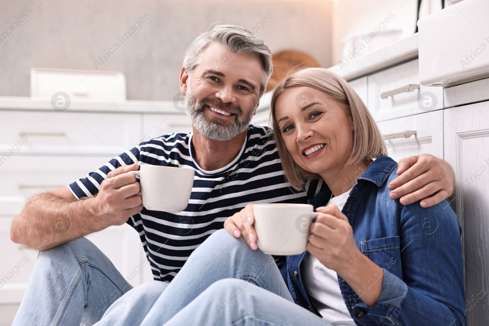 Photo of Happy middle aged couple with cups of drink in kitchen