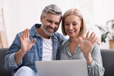 Photo of Happy middle aged couple having video chat via laptop on sofa indoors