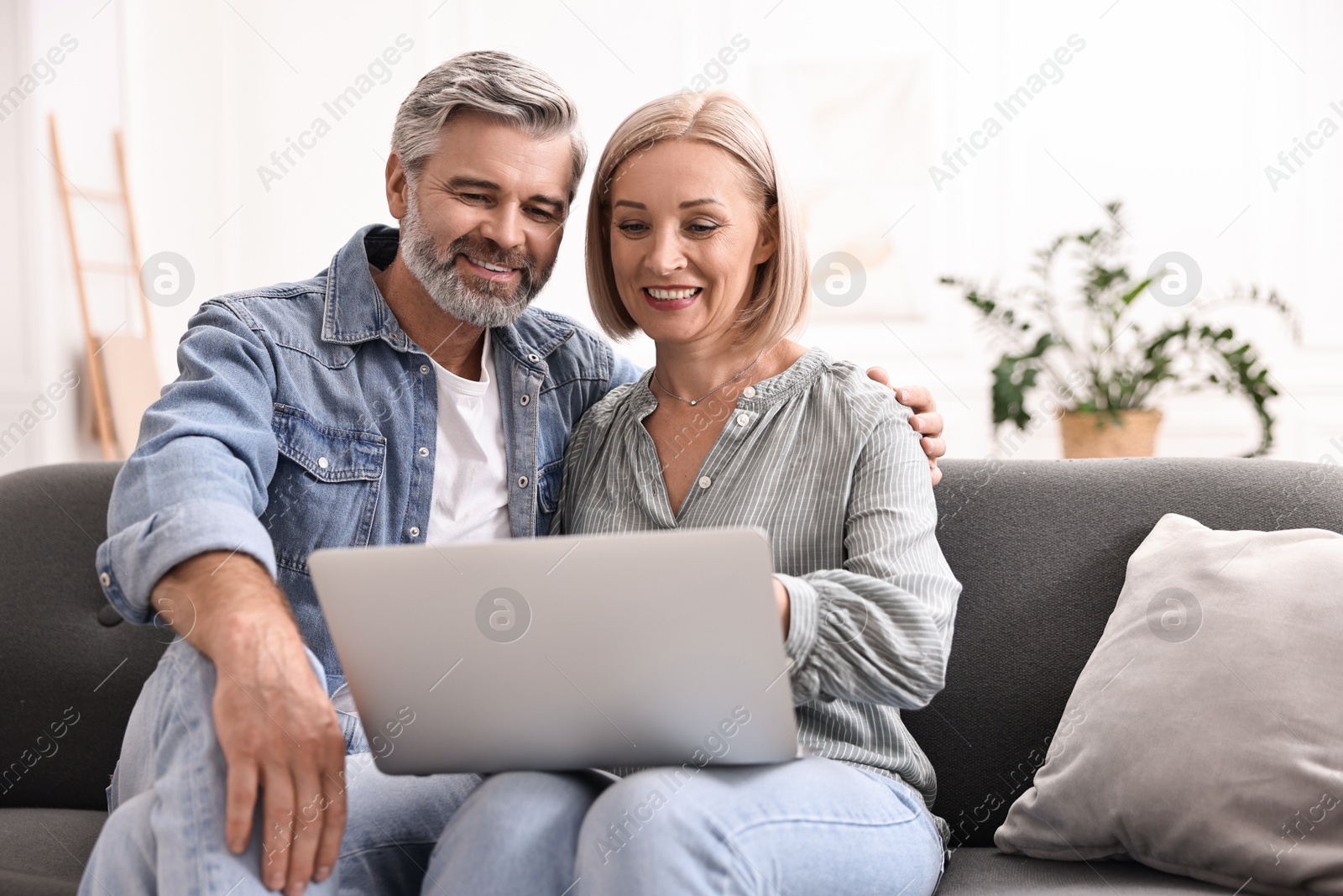 Photo of Happy middle aged couple using laptop on sofa at home