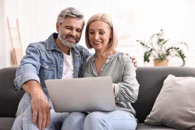 Happy middle aged couple using laptop on sofa at home