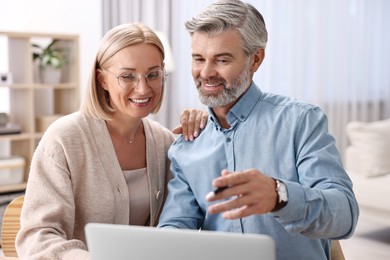 Photo of Happy middle aged couple using laptop at home