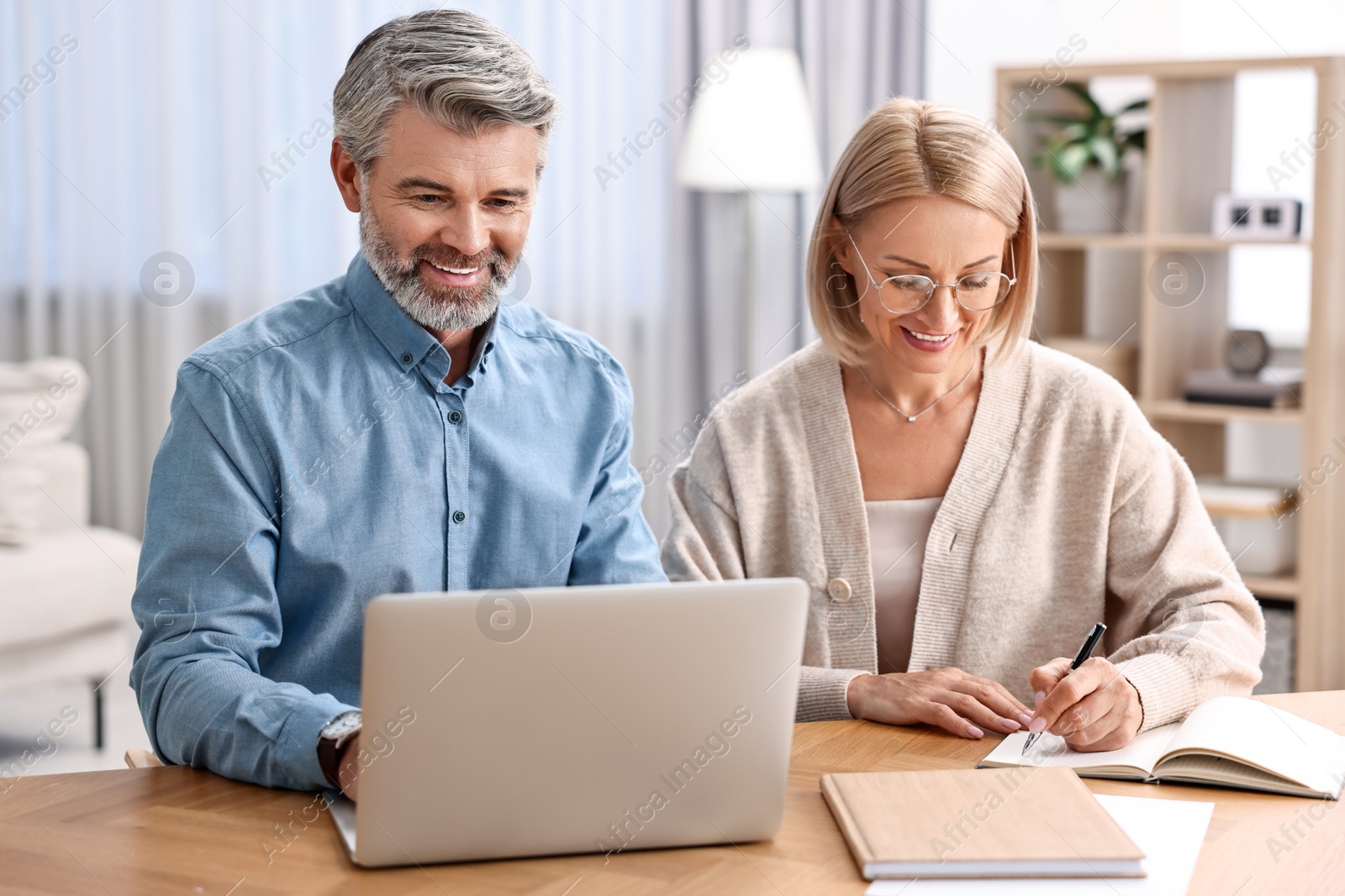 Photo of Happy middle aged couple working at wooden table indoors