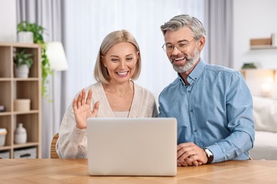 Happy middle aged couple having video chat via laptop at wooden table indoors