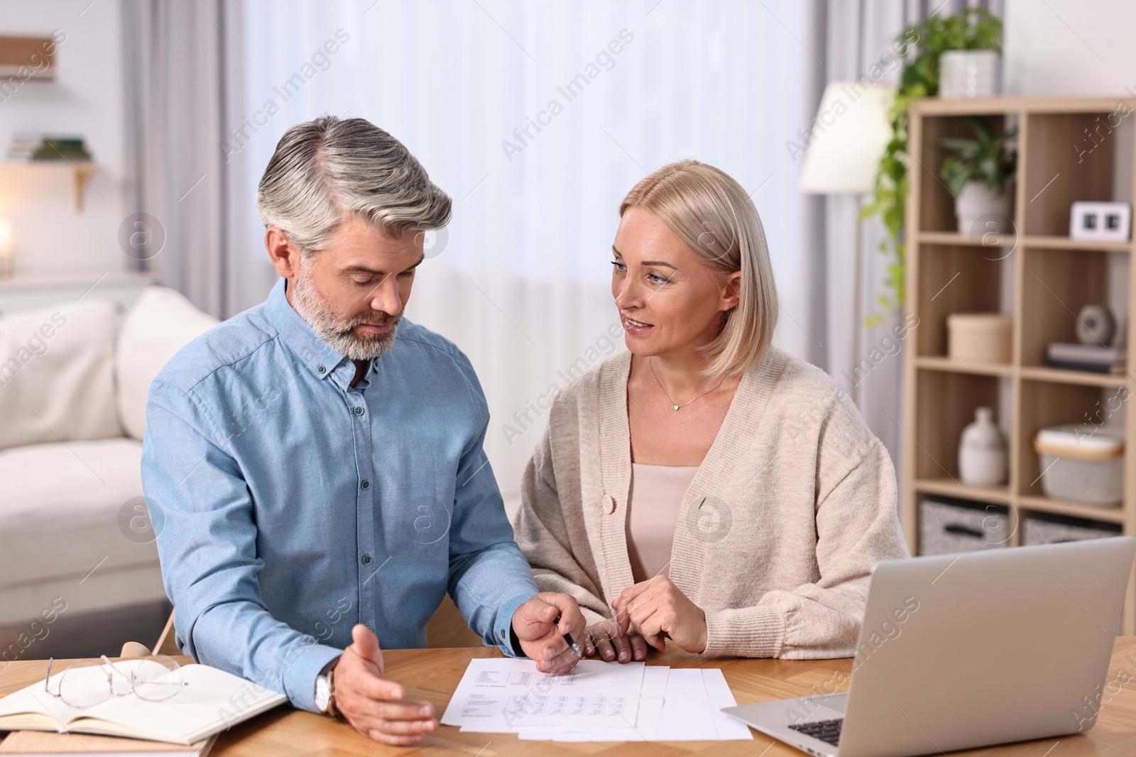 Photo of Middle aged couple working at wooden table indoors