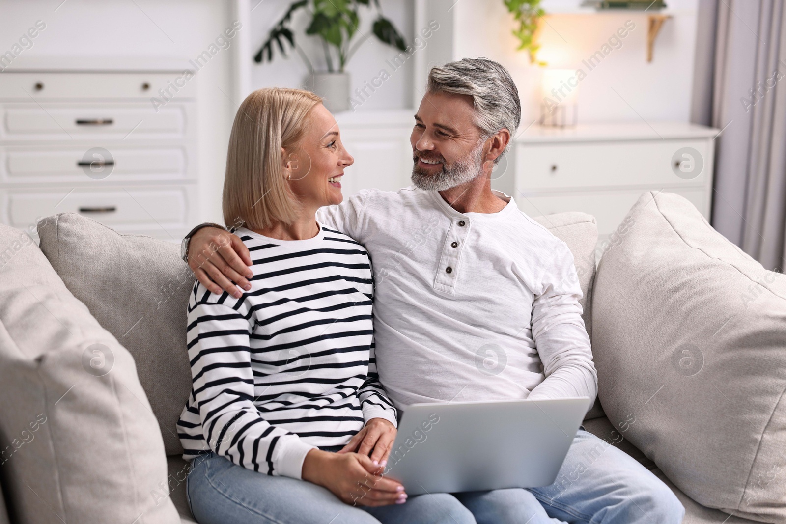 Photo of Happy middle aged couple using laptop on sofa at home