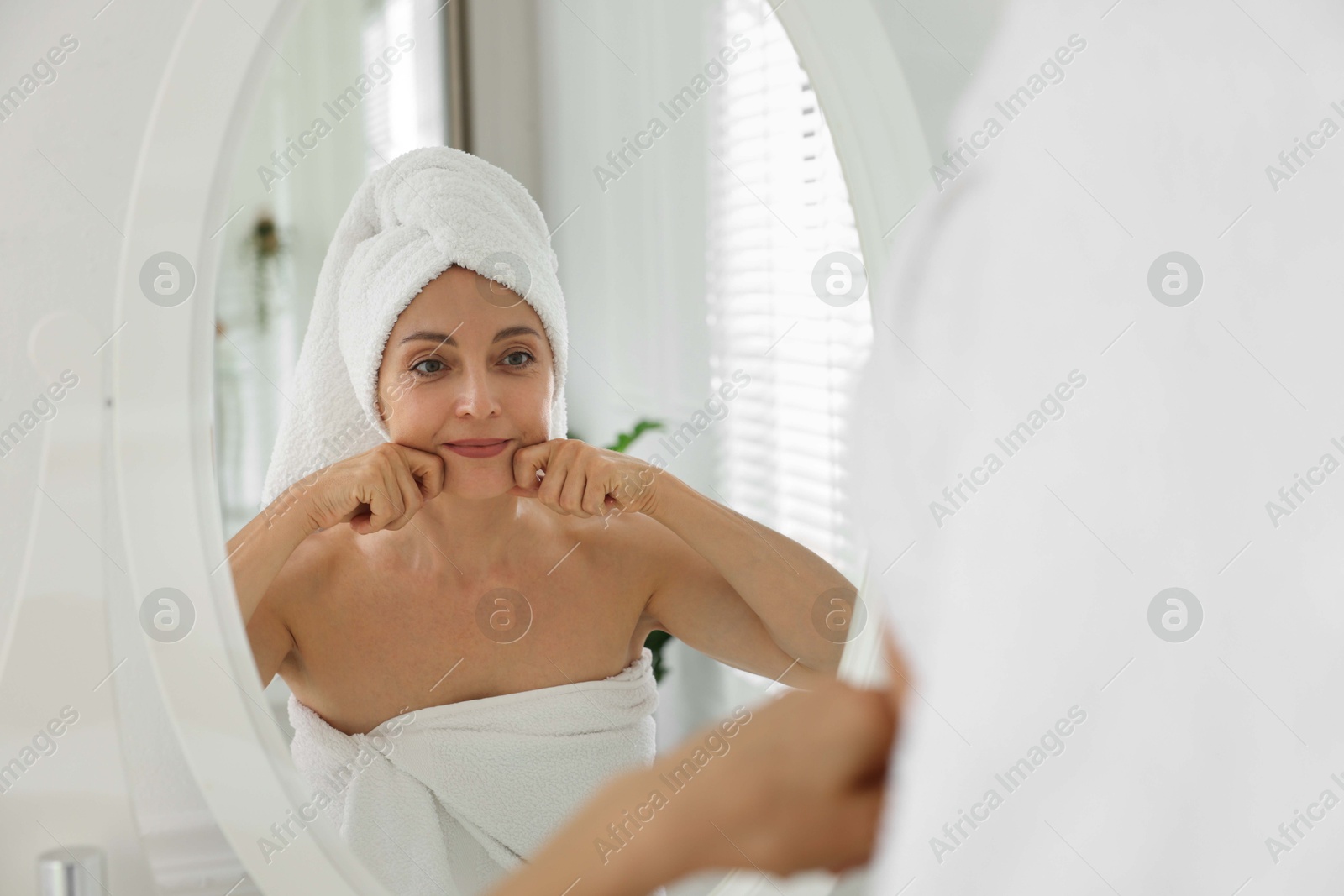 Photo of Beautiful woman doing facial self massage near mirror in bathroom