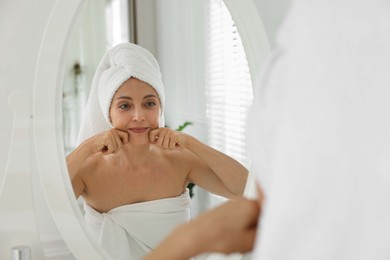 Photo of Beautiful woman doing facial self massage near mirror in bathroom