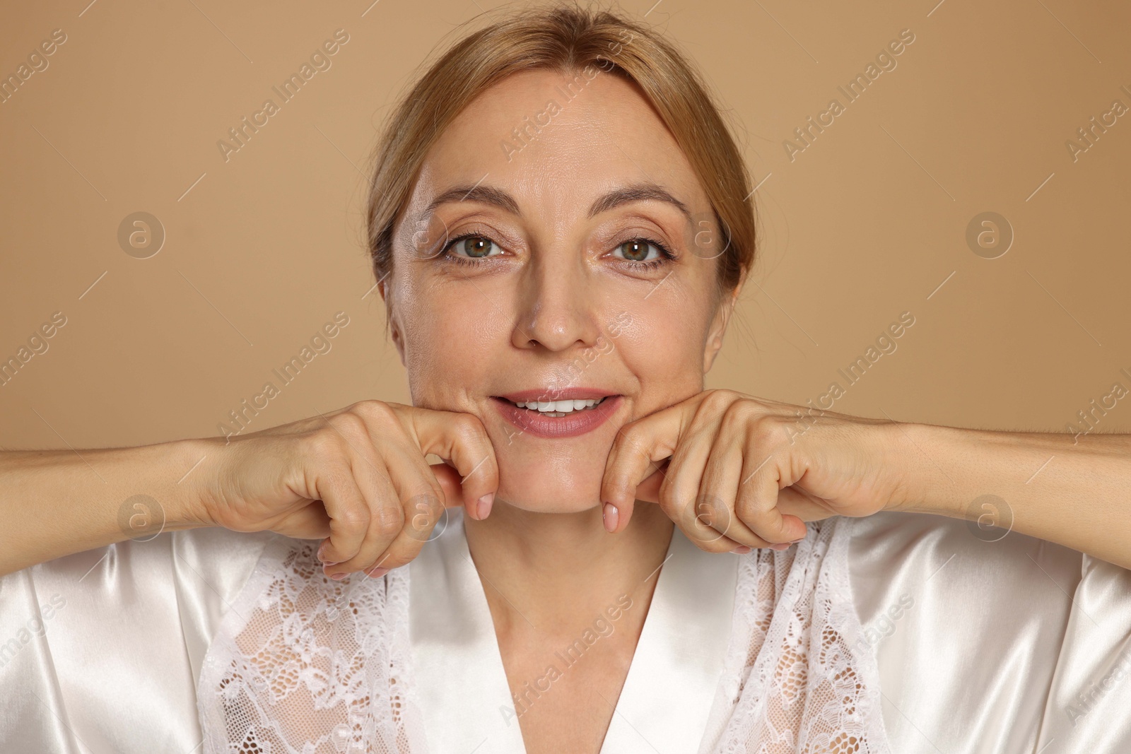 Photo of Smiling woman doing facial self massage on beige background