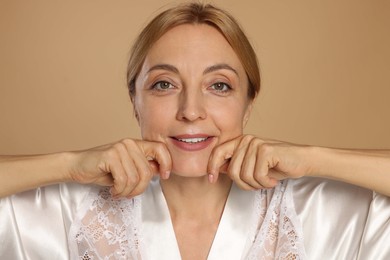 Photo of Smiling woman doing facial self massage on beige background