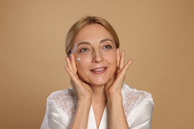 Smiling woman with cream on face against beige background