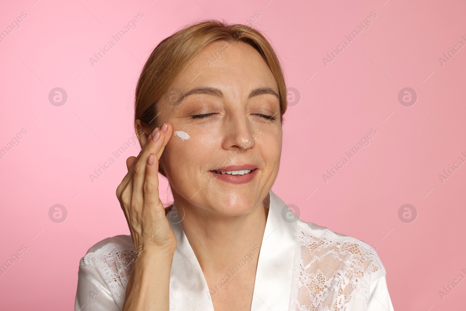 Photo of Smiling woman with cream on face doing self massage against pink background