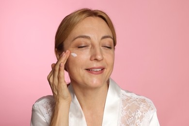 Smiling woman with cream on face doing self massage against pink background