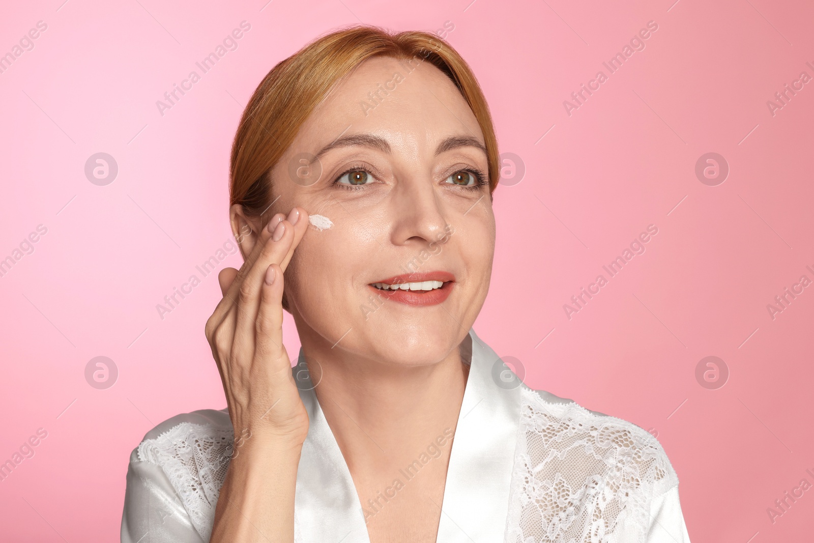 Photo of Smiling woman with cream on face doing self massage against pink background