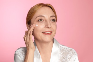 Smiling woman with cream on face doing self massage against pink background